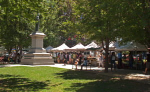Shoppers moving between produce stalls at a California farmers market on a summer morning.