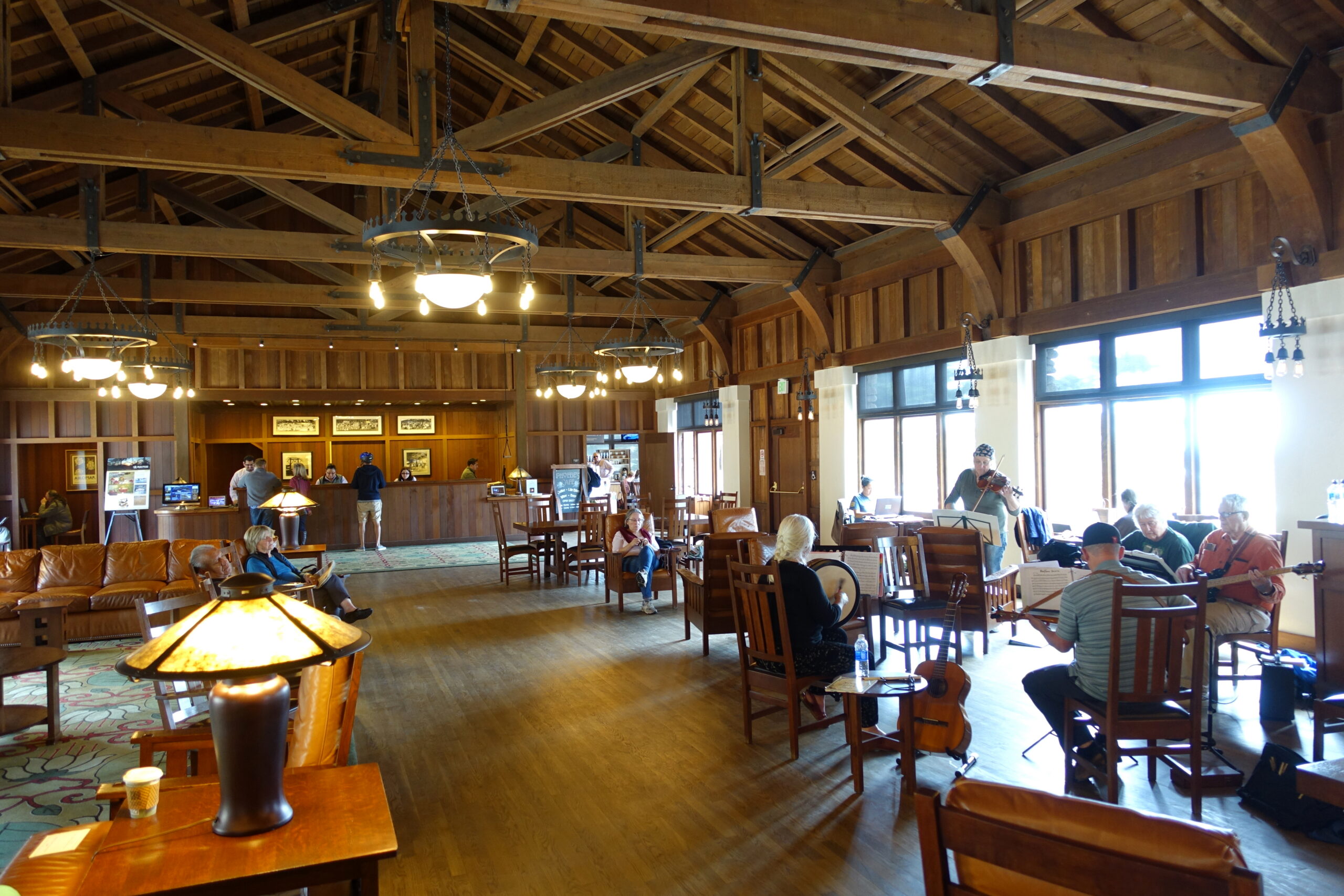 The interior of Julia Morgan's 1913 Social Hall at Asilomar, redwood trusses arching overhead above Arts-and-Crafts chandeliers and oak furniture